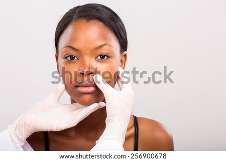 doctor checking african woman lips before plastic surgery on plain background