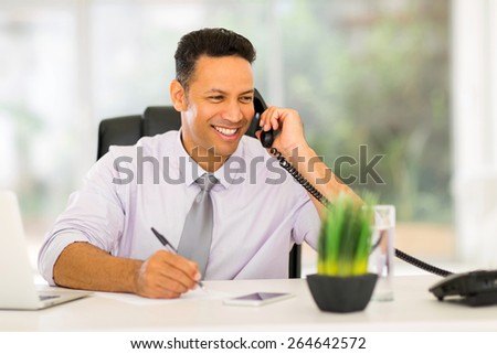 smiling middle aged businessman talking on landline phone and writing report
