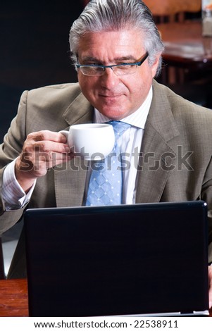 Portrait of a happy senior business man sitting by his laptop and drinking coffee