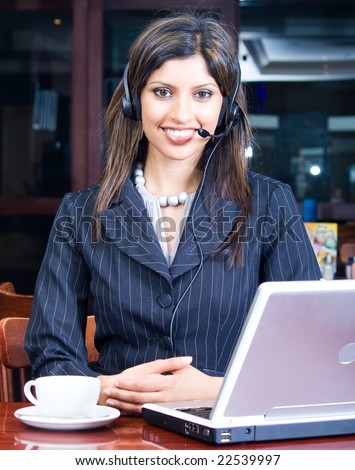 closeup of smiling indian business woman with headset and laptop in a cafe