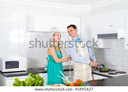 happy young wife help husband tie up apron in kitchen