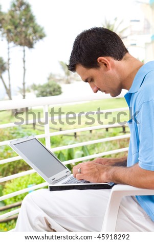 casual young man using laptop on balcony with sea view behind