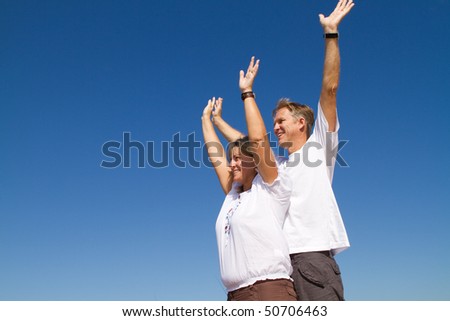 happy positive mature couple arms open, background is blue sky
