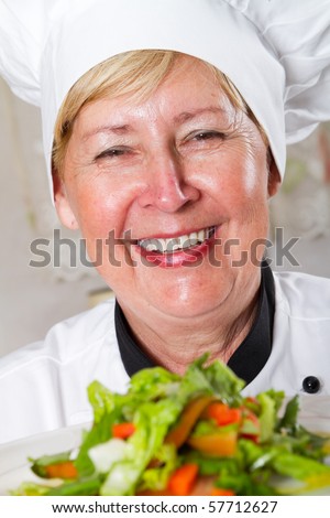 professional senior female chef in kitchen presenting salad