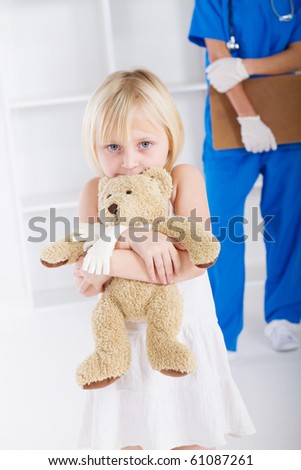 little girl holding teddy bear in doctor\'s office