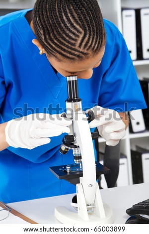 african american female lab technician looking through microscope in lab