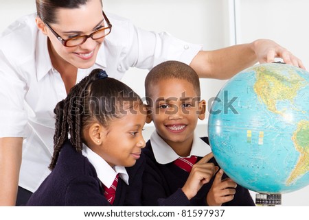 elementary geography teacher and students looking at globe in classroom