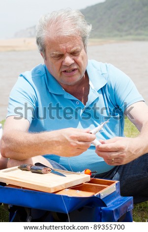 senior man by the lake putting bait on fishing hook