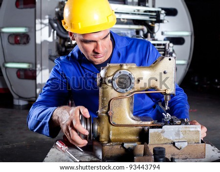 male technician fixing industrial sewing machine in factory