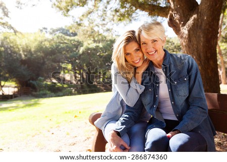 attractive mid age mother and daughter sitting on a bench outdoors