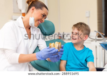 friendly female dentist explaining teeth model to little patient at clinic