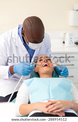 african american dentist cleaning and polishing teeth of a patient