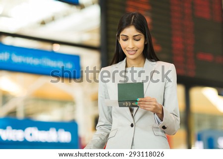 young businesswoman looking at boarding pass in front of flight information board at airport