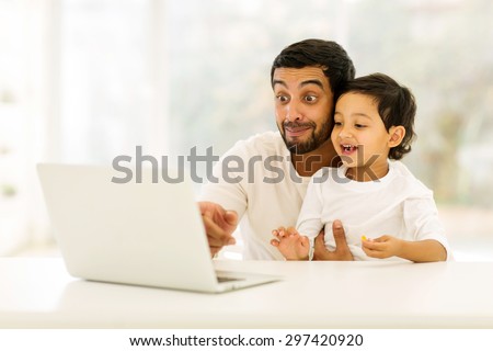 playful young indian man using laptop with his son at home