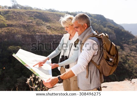active middle aged hikers looking at a map on top of the mountain