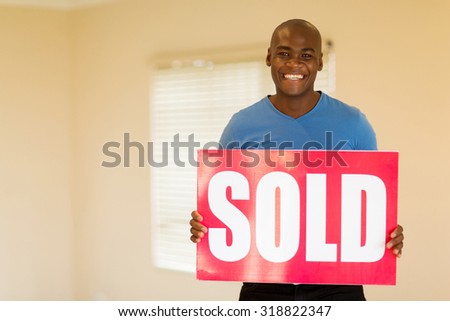 happy young black man holding sold sign in his home