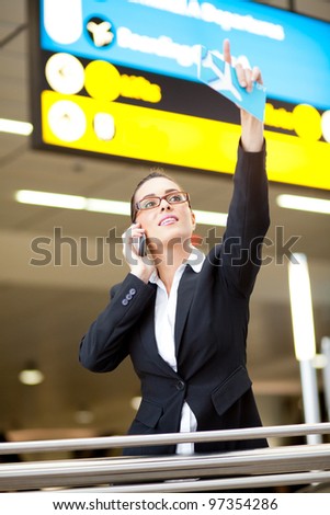 young businesswoman waving to someone while talking on cell phone at airport