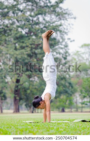 Beautiful woman practicing yoga in the park. Handstand/ Adho Mukha Vrksasana.