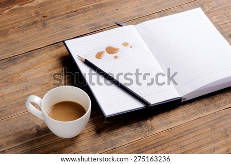 Coffee in cup drop on the white page notebook and pencil