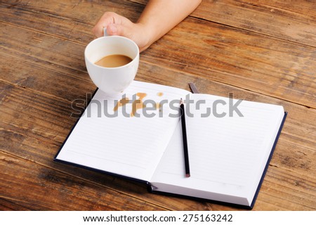 Coffee in cup drop on the white page notebook and pencil