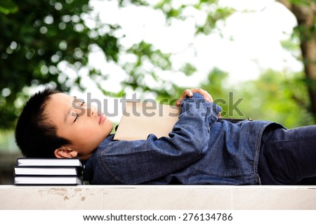 Young boy sleeping with books in the garden