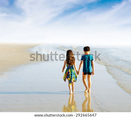 Brother sister holding hand walk on the beach in tropical seaside under blue sky white cloud