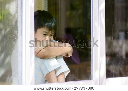 Asian boy sit beside window after rain at home look sad and lonely on dark room background.
