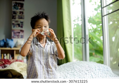Close up young asian boy drink water from transparent glass after wake up in the morning from the bed