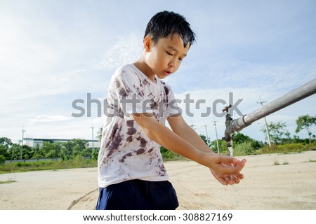 Close up Asian boy take water from old faucet on hot and dry empty land. Water shortage and drought concept.