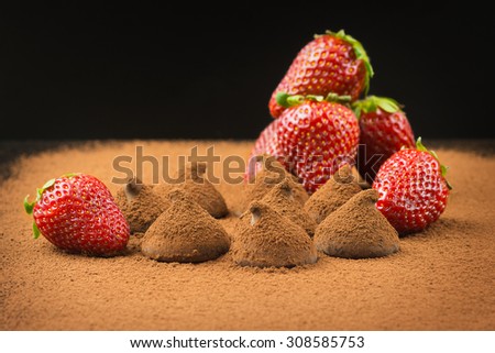 Chocolate truffles, strawberries and cocoa powder on a black background.