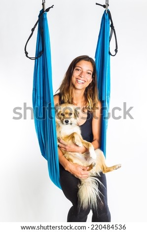 Young woman posing with a small dog while doing anti-gravity aerial yoga in hammock on a seamless white background.