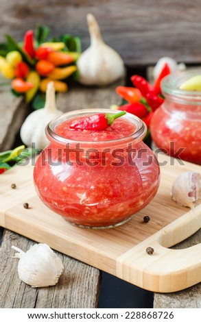 Adjika - homemade sauce of fresh tomatoes, red peppers and spices in glass can on wooden background