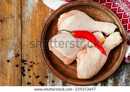 Fresh raw chicken legs in clay plate on wooden background with ukrainian style decorations