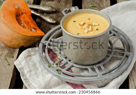 Pumpkin soup in vintage iron cup on iron support with fresh pumpkins and wooden background
