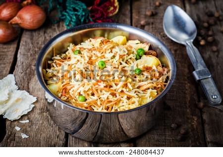 Biryani with chicken and vegetables in iron bowl on vintage wooden background