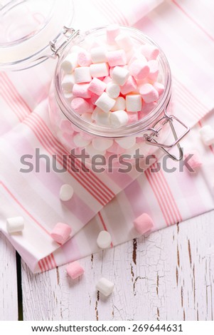 Pink and white small marshmallows in a glass pot on wooden table. Selective focus