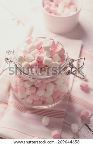 Pink and white small marshmallows in a glass pot on wooden table. Selective focus. Toned image