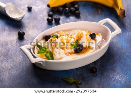 Delicious banana split with blueberry, mint, almonds and sauce on blue wooden background. Selective focus