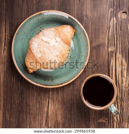 Fresh croissant and mug of black coffee on wooden table. Top view. Vintage style
