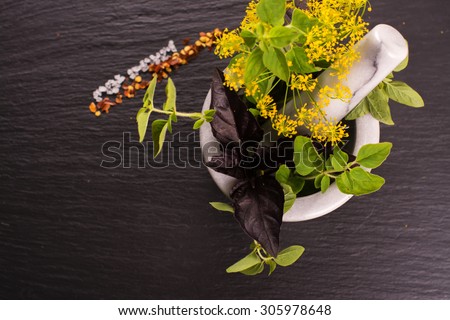 Fresh organic herbs: dill, oregano and basil in a marble mortar. Seasonings on black stone background. Selective focus. Top view