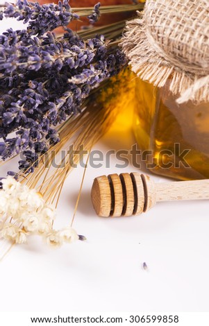 Golden lavender honey in a glass jar with dry herbs on light background. Autumn or harvest concept. Selective focus. Toned image