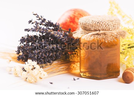 Golden lavender honey in a glass jar with dry herbs on light background. Autumn or harvest concept. Selective focus. Toned image