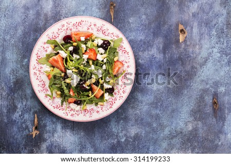 Diet or vegetarian concept. Fresh salad with arugula, cherry, strawberry, feta cheese on blue rustic background. Top view. Selective focus