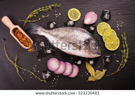 Fresh raw dorada fish with lime, red onion, spices and herbs over black stone background. Toned image