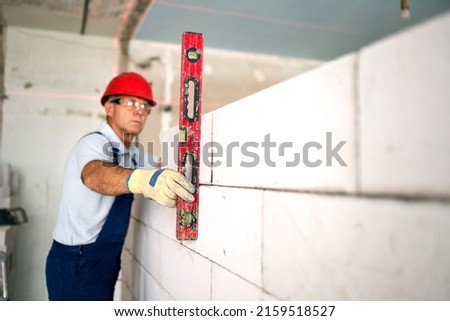 Similar – Foto Bild Arbeiter baut Mauer mit roten Blöcken und Mörtel