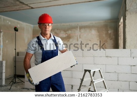 Similar – Foto Bild Arbeiter baut Mauer mit roten Blöcken und Mörtel