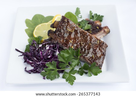 Smoked Barbecue Baby Back Ribs decorated with Spinach Red Cabbage Lemon and Parsley in a White Ceramic Plate