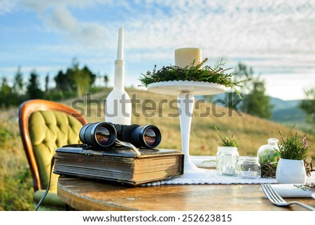 Vintage decor for photo session in the mountains: table with book, candlesticks and binoculars