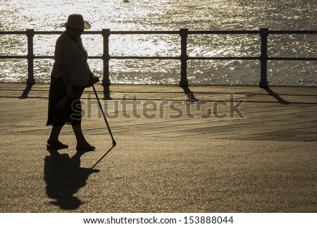 Old woman with hat and cane walking at sunset