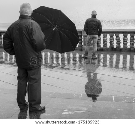 Old man with umbrella and young man contemplating the sea